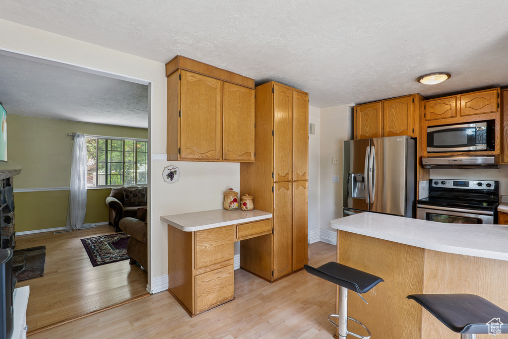 Kitchen featuring stainless steel appliances, light countertops, light wood finished floors, a breakfast bar area, and under cabinet range hood