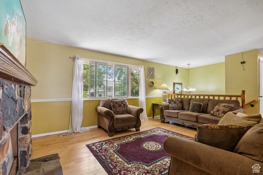 Living room featuring a stone fireplace, light wood-type flooring, a chandelier, and a textured ceiling