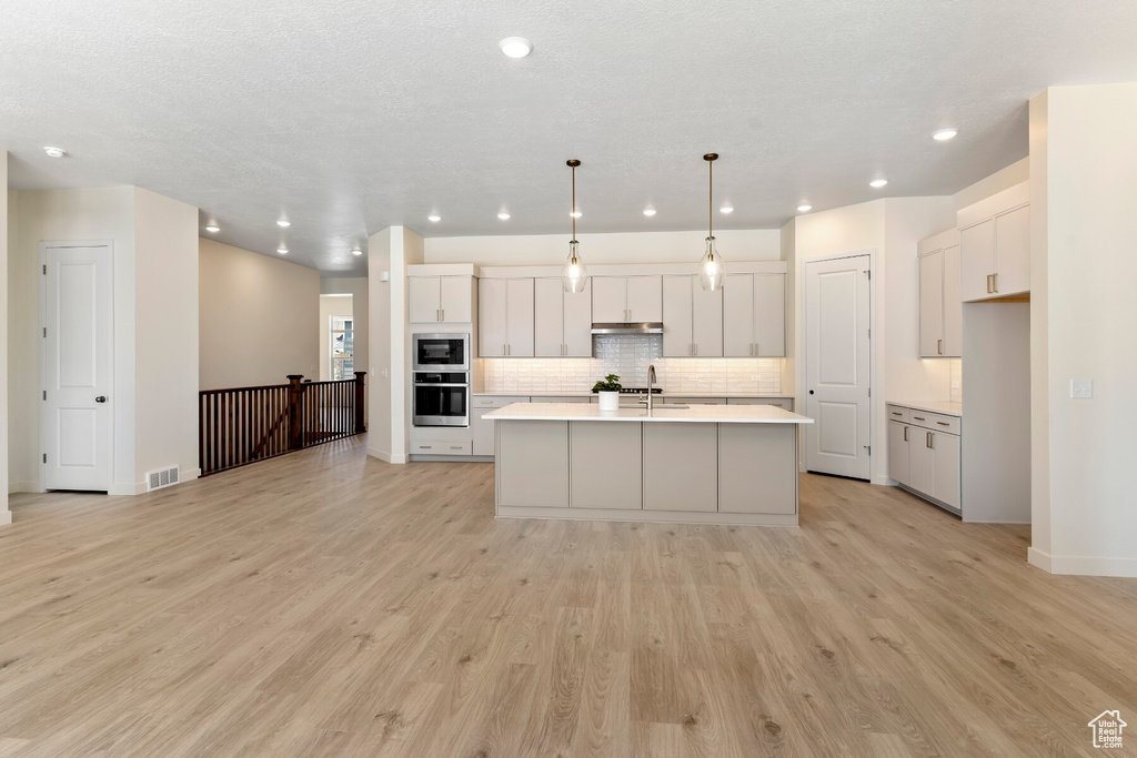 Kitchen featuring stainless steel oven, built in microwave, light countertops, tasteful backsplash, and light wood finished floors
