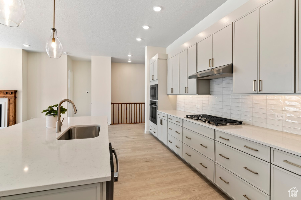 Kitchen with appliances with stainless steel finishes, under cabinet range hood, backsplash, light wood-style floors, and recessed lighting