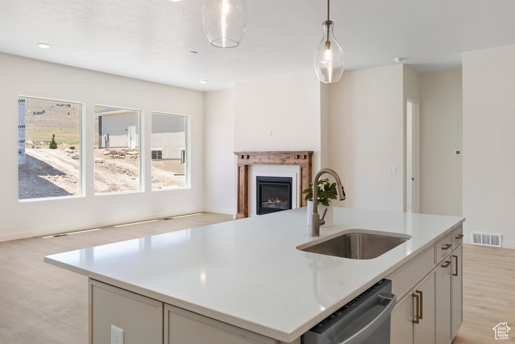 Kitchen with stainless steel dishwasher, open floor plan, light wood finished floors, pendant lighting, and a glass covered fireplace