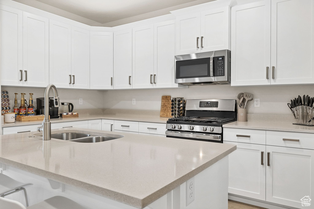 Kitchen with appliances with stainless steel finishes, a center island with sink, white cabinetry, light stone counters, and a kitchen bar