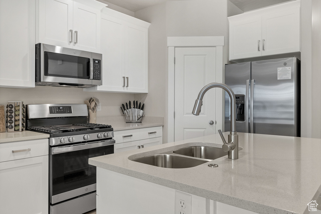 Kitchen featuring stainless steel appliances, white cabinets, an island with sink, and light stone countertops