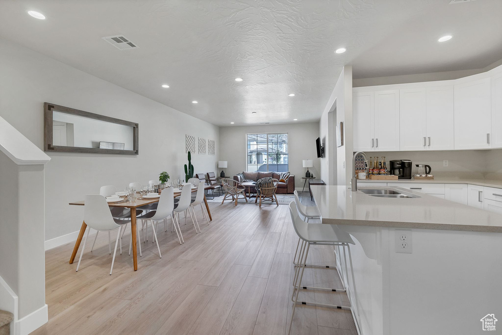 Kitchen with light wood-style flooring, recessed lighting, white cabinetry, open floor plan, and a kitchen breakfast bar