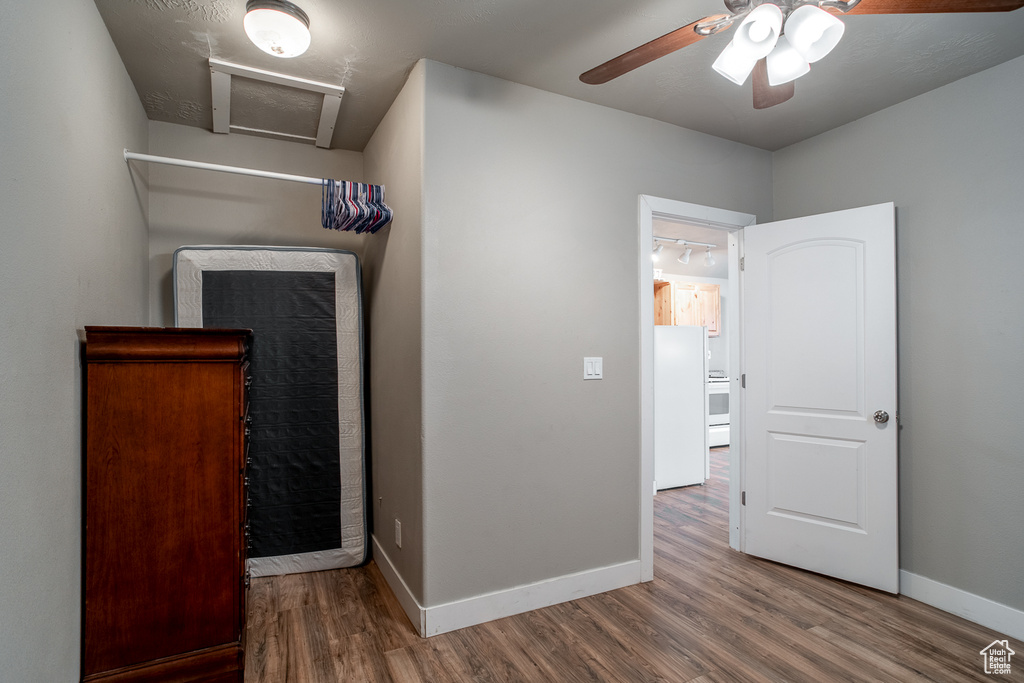 Unfurnished bedroom with freestanding refrigerator, wood finished floors, attic access, and a ceiling fan
