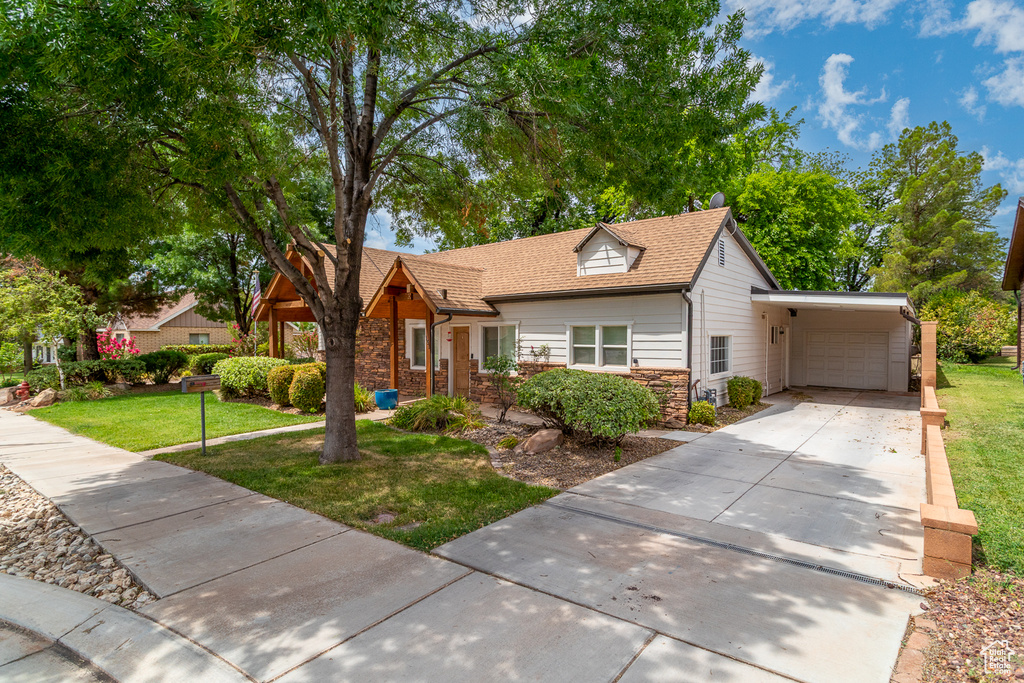 View of front of home featuring stone siding, an attached garage, a front lawn, and driveway
