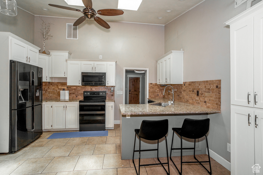 Kitchen featuring black appliances, a peninsula, tasteful backsplash, ceiling fan, and a high ceiling