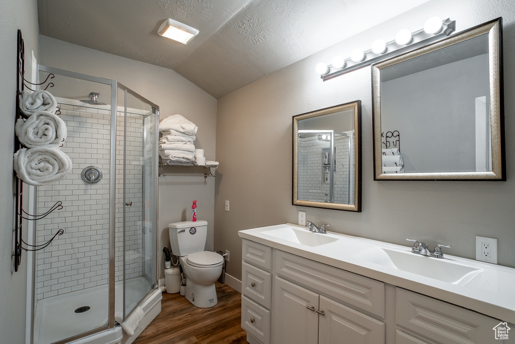 Full bath featuring wood finished floors, double vanity, a shower stall, and vaulted ceiling