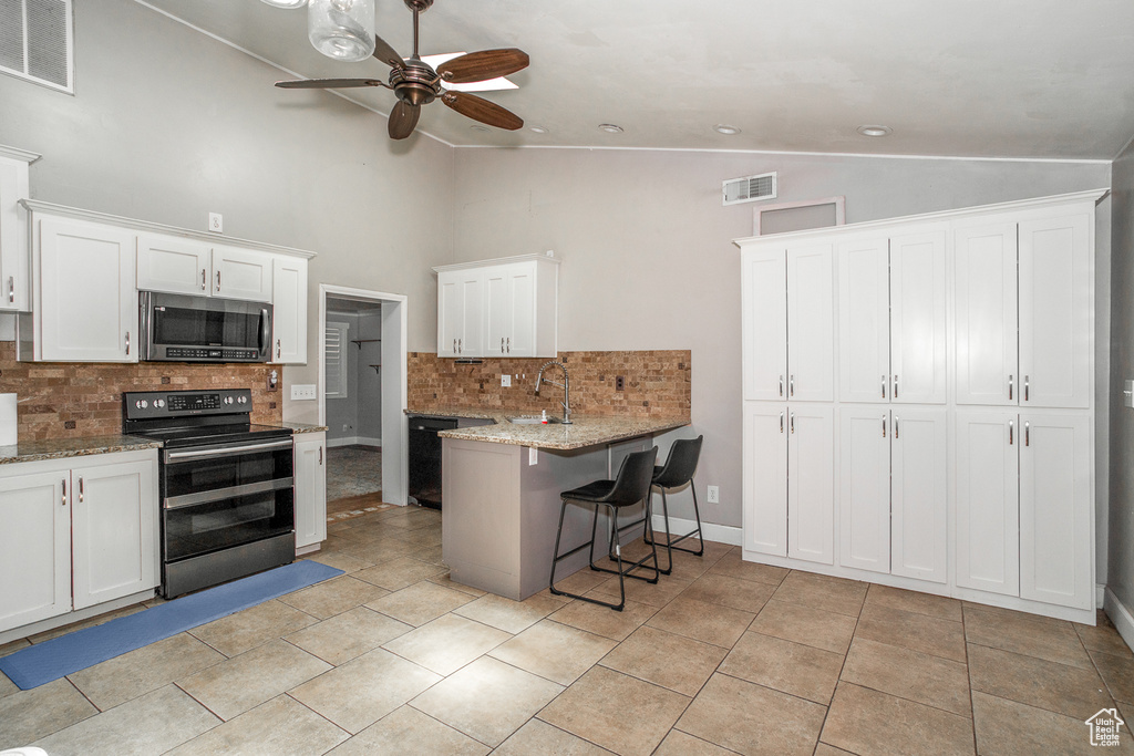 Kitchen with appliances with stainless steel finishes, vaulted ceiling, ceiling fan, decorative backsplash, and white cabinetry