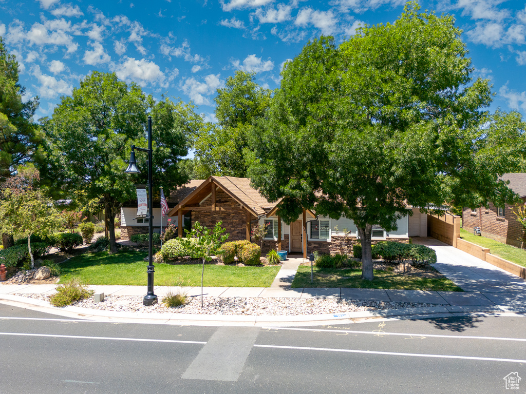 View of property hidden behind natural elements with stone siding, concrete driveway, a front lawn, and an attached carport