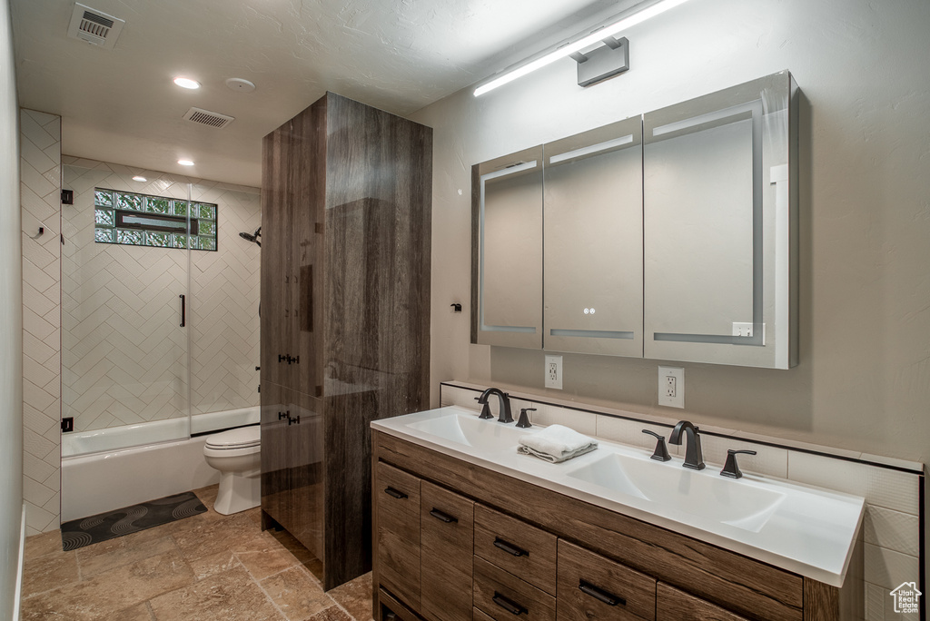 Bathroom with stone tile flooring, double vanity, shower / bath combination with glass door, and recessed lighting