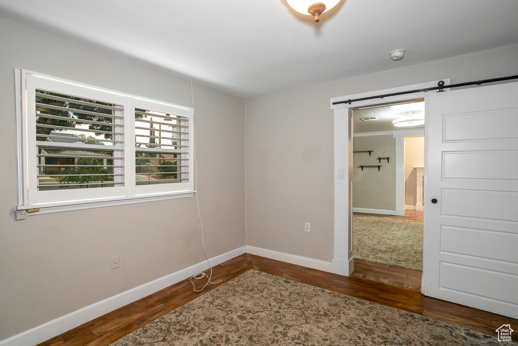Unfurnished room with wood finished floors, a barn door, and a smoke detector