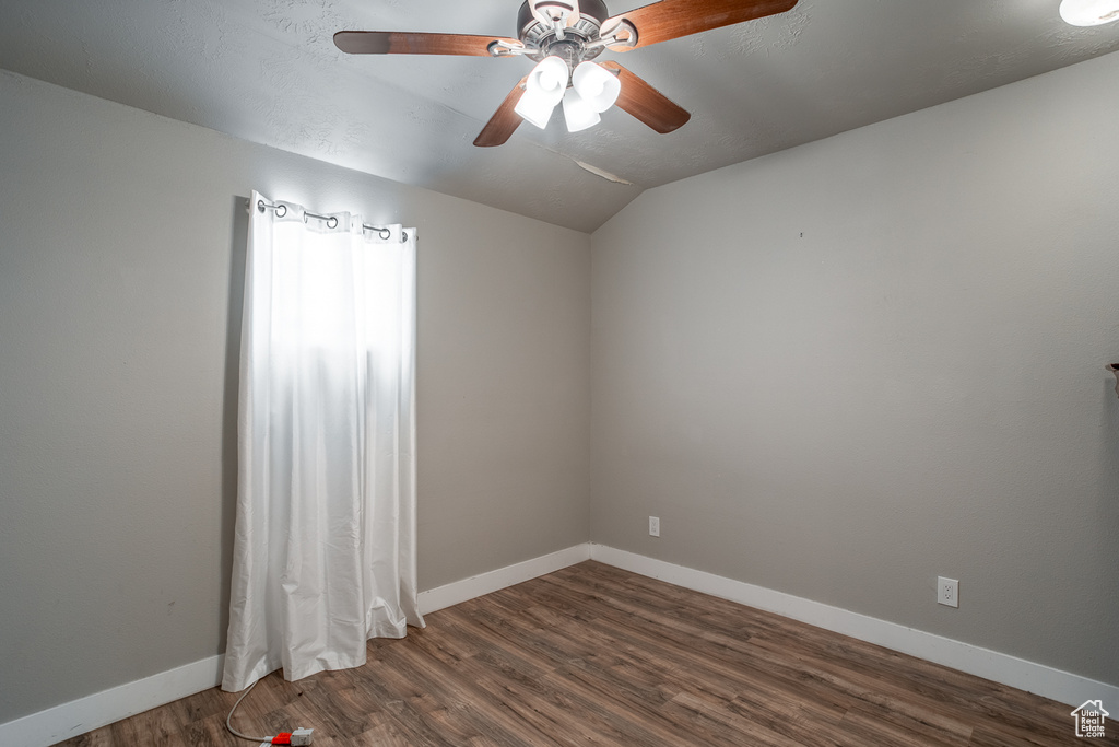 Empty room with lofted ceiling, ceiling fan, and dark wood-style floors