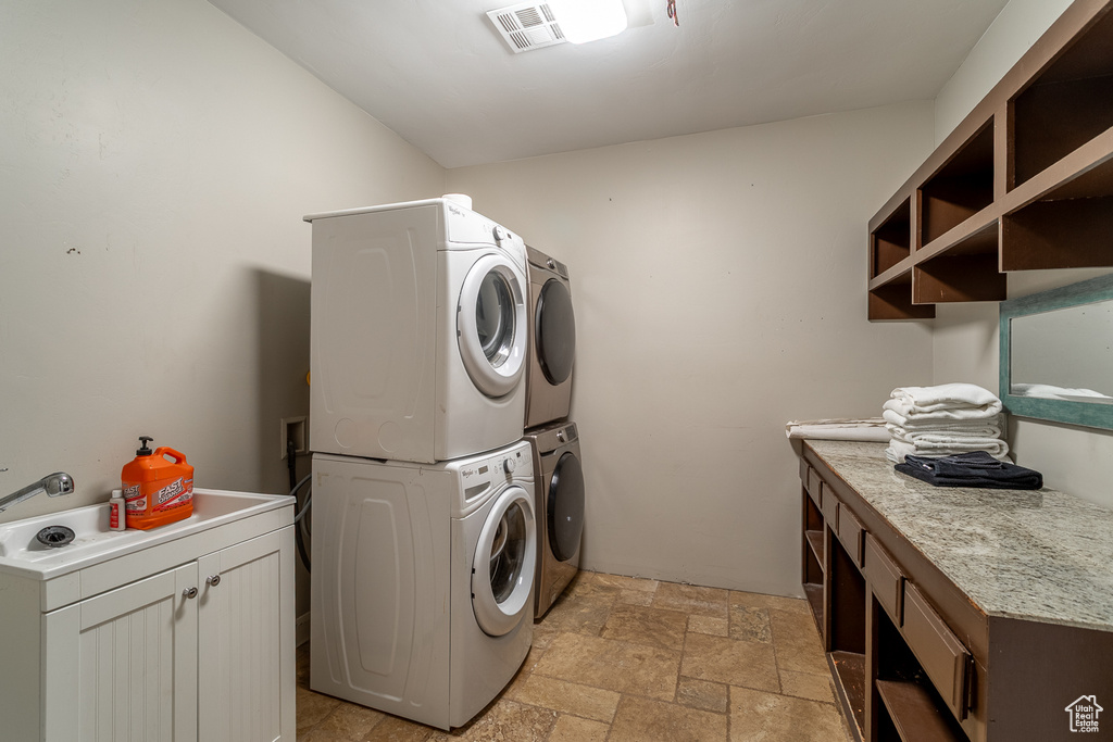 Laundry area with stacked washer and clothes dryer, cabinet space, and stone tile floors