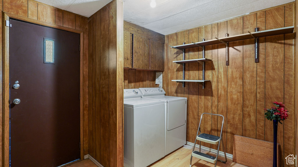 Washroom with separate washer and dryer, light wood-style flooring, wood walls, and cabinet space