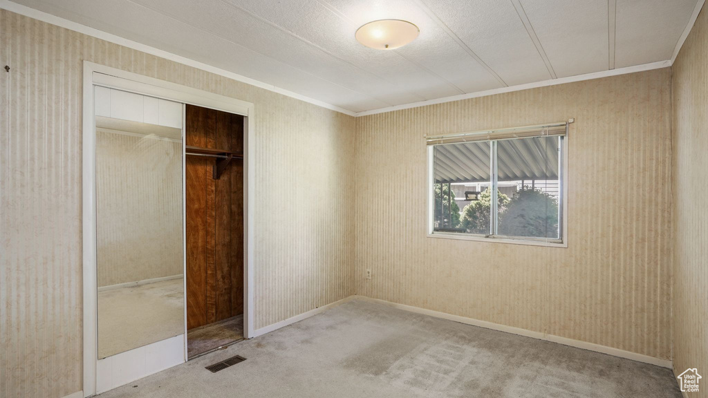 Unfurnished bedroom with ornamental molding, carpet, a closet, and wallpapered walls
