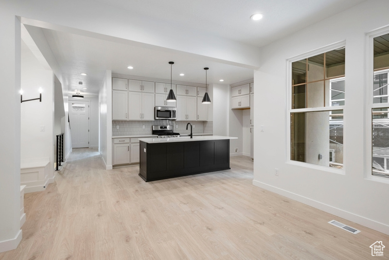Kitchen featuring stainless steel appliances, light countertops, decorative backsplash, recessed lighting, and light wood-style flooring