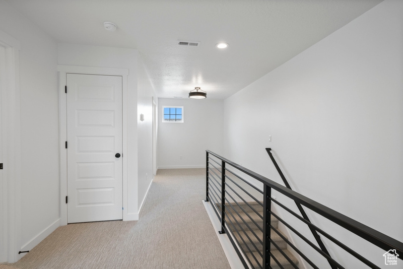 Hall with an upstairs landing, carpet flooring, and recessed lighting