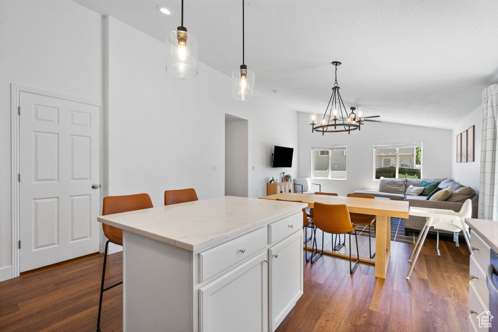 Kitchen featuring vaulted ceiling, a chandelier, dark wood finished floors, white cabinetry, and a breakfast bar area