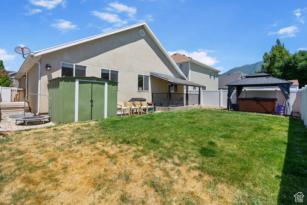 Back of property featuring a shed, a hot tub, a fenced backyard, and stucco siding