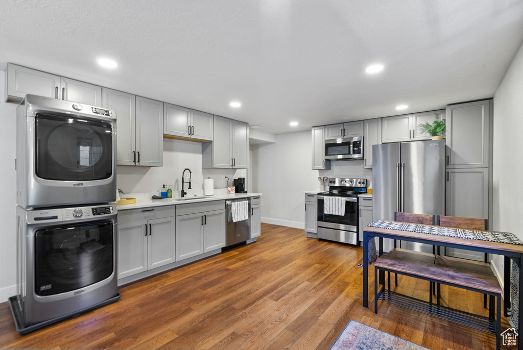Kitchen featuring stainless steel appliances, stacked washer / dryer, gray cabinets, light countertops, and wood finished floors