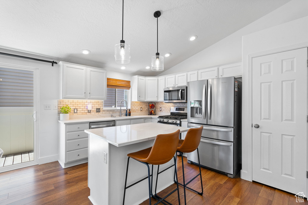 Kitchen featuring appliances with stainless steel finishes, decorative backsplash, dark wood-style floors, lofted ceiling, and white cabinets