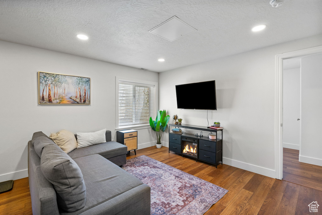 Living room with a textured ceiling, wood finished floors, recessed lighting, and a glass covered fireplace