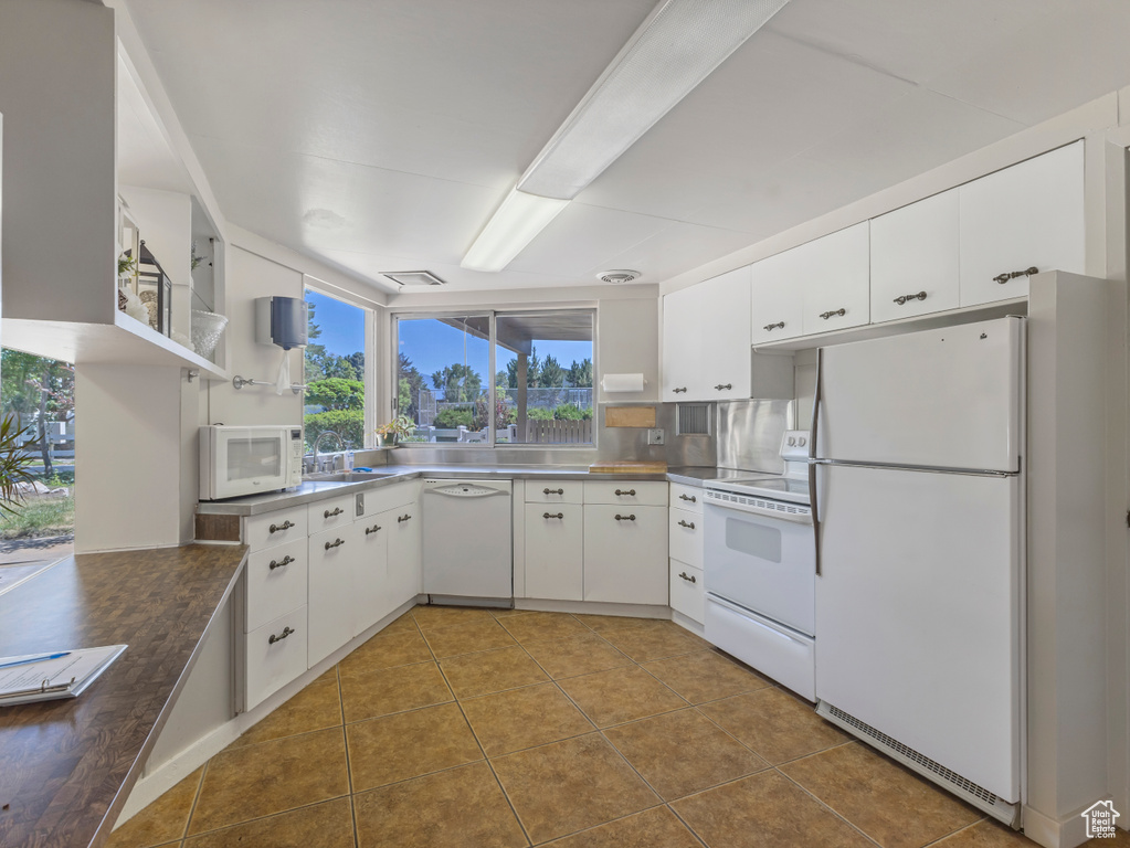Kitchen with stainless steel countertops, white appliances, white cabinets, dark tile patterned floors, and open shelves