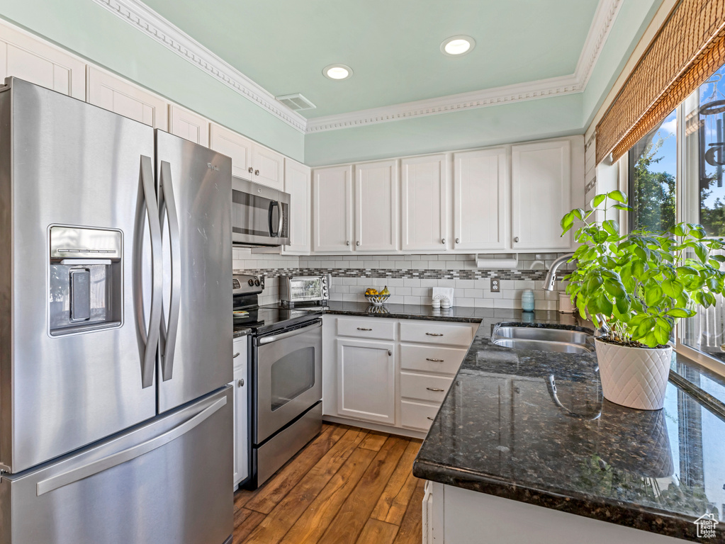 Kitchen featuring stainless steel appliances, white cabinetry, ornamental molding, dark stone counters, and tasteful backsplash