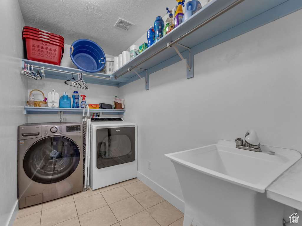 Laundry room with washing machine and clothes dryer, tile patterned floors, and a textured ceiling