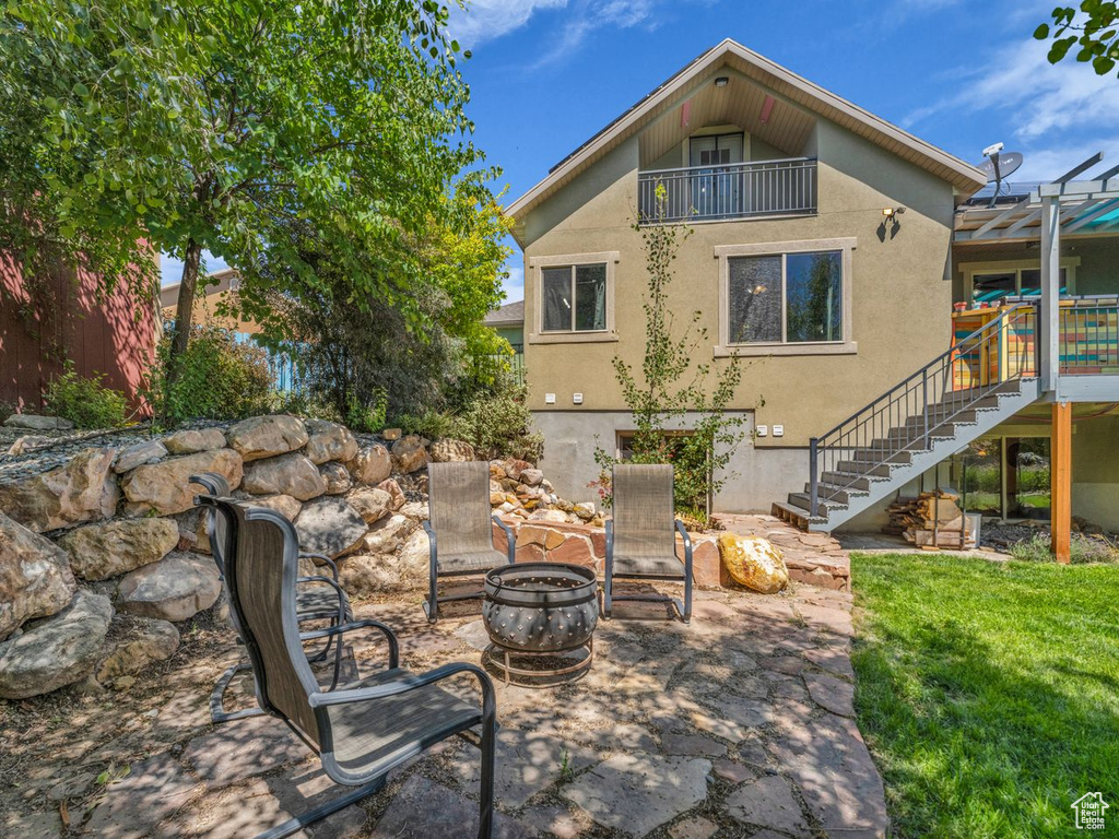 Back of house with stucco siding, an outdoor fire pit, stairs, a patio, and a balcony
