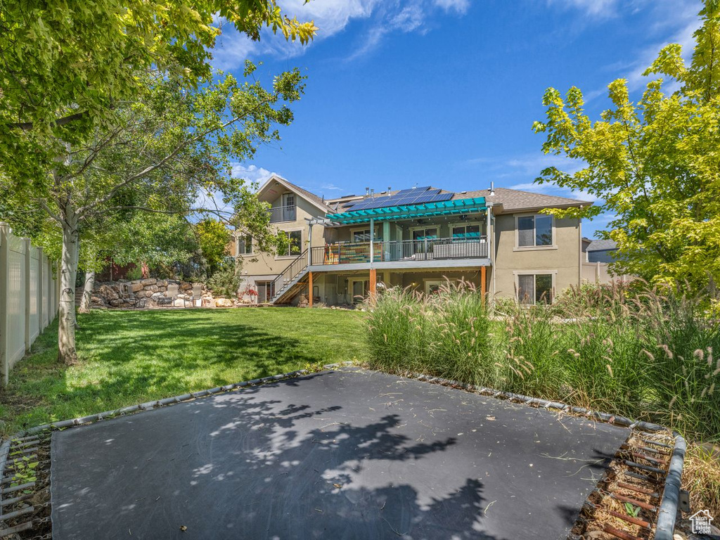 Rear view of property with stairway, a yard, a wooden deck, solar panels, and stucco siding
