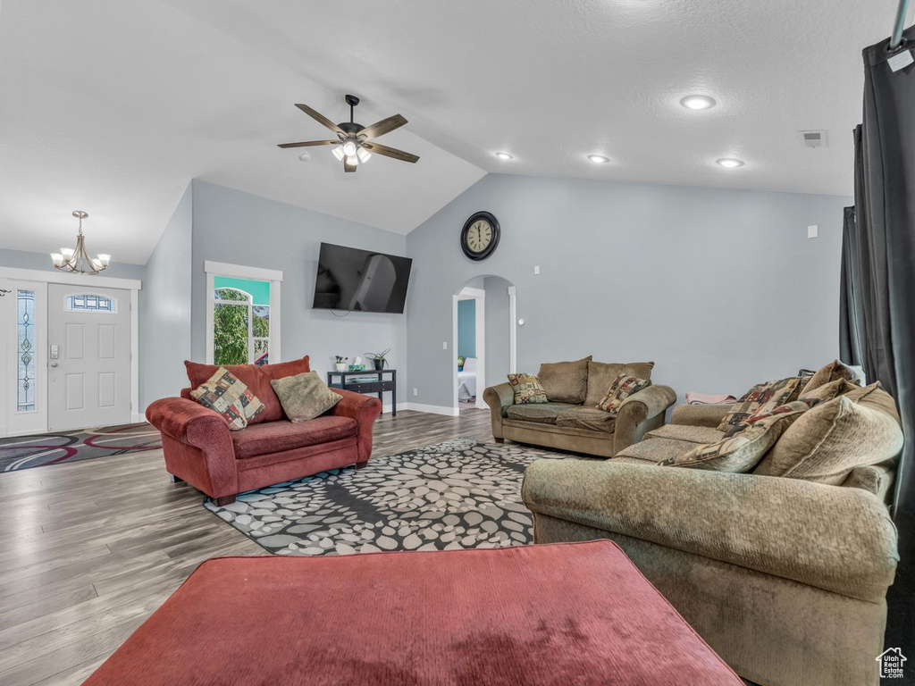 Living area with wood finished floors, vaulted ceiling, arched walkways, a chandelier, and a ceiling fan