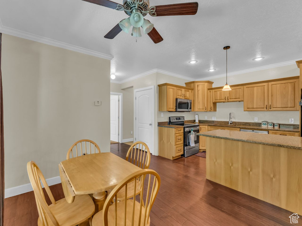 Kitchen with appliances with stainless steel finishes, a ceiling fan, ornamental molding, dark wood finished floors, and dark stone countertops