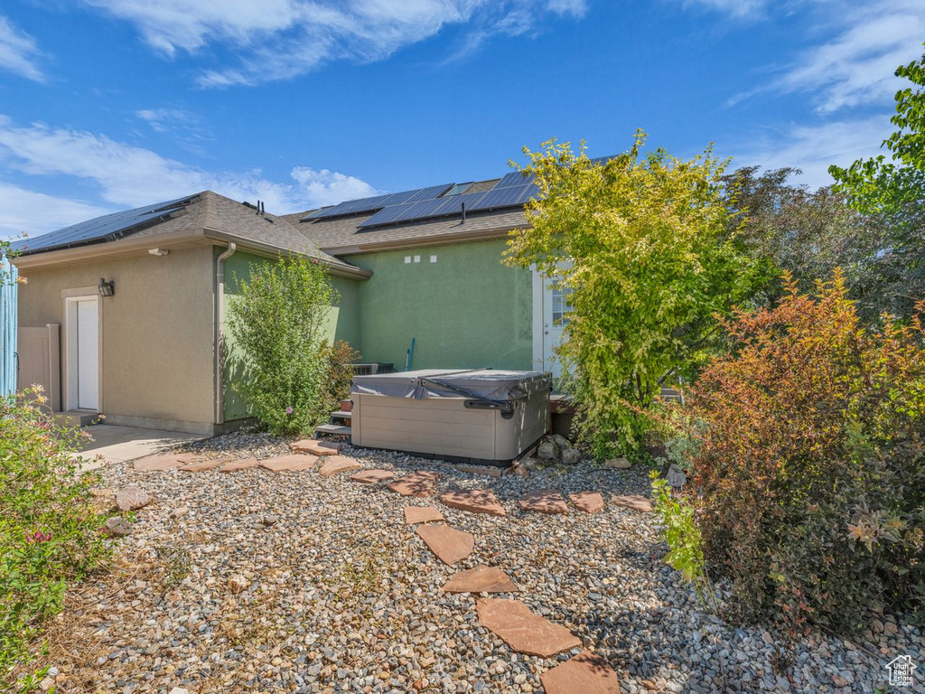 View of side of home featuring a hot tub, solar panels, stucco siding, and a shingled roof