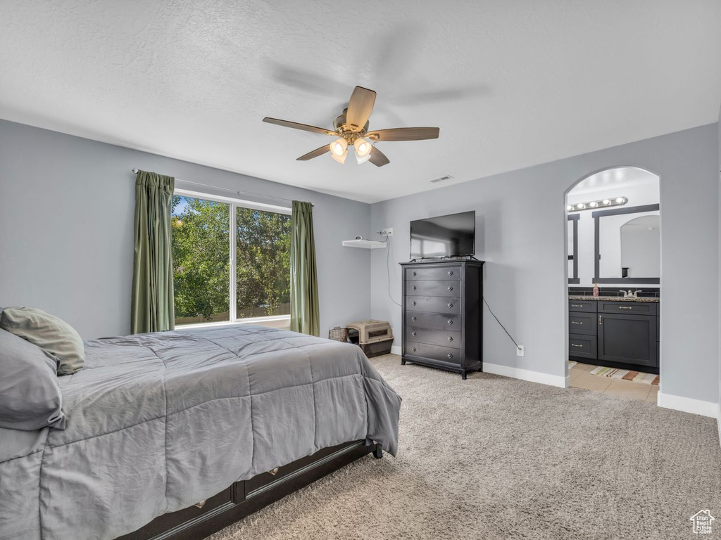 Bedroom with light colored carpet, arched walkways, ensuite bath, and ceiling fan