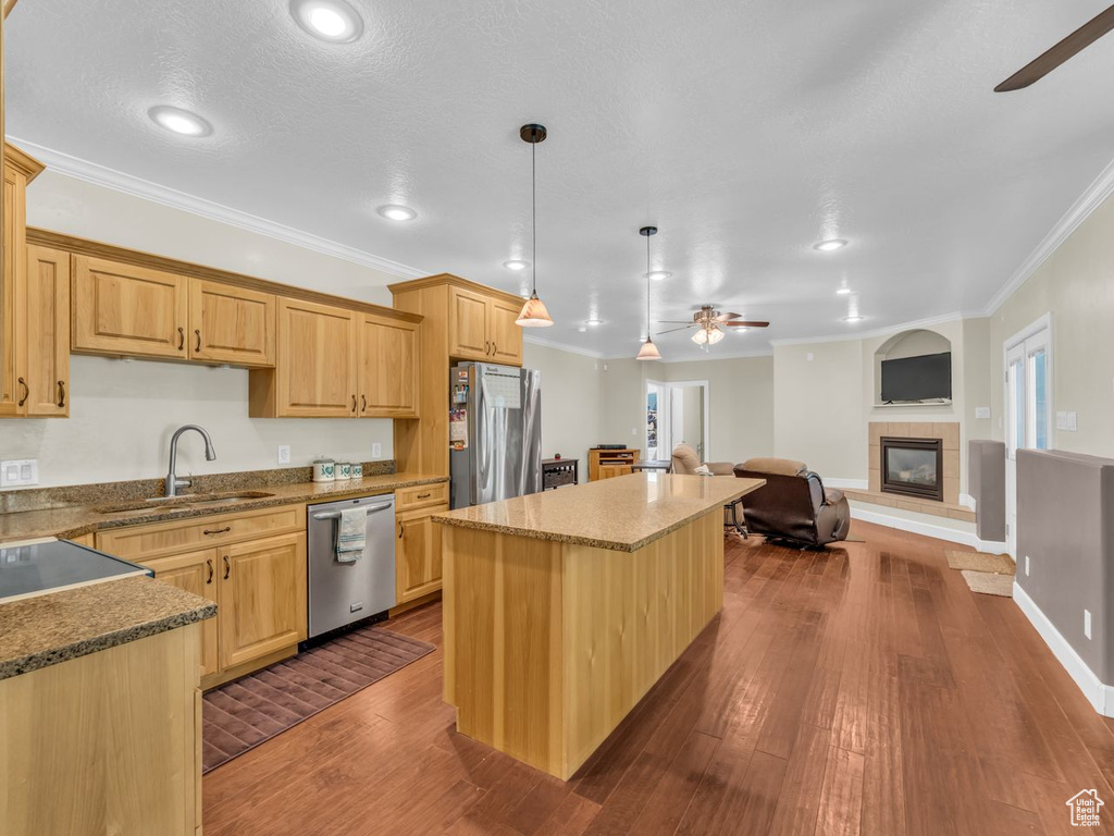 Kitchen featuring stainless steel appliances, ceiling fan, crown molding, a tiled fireplace, and a kitchen island