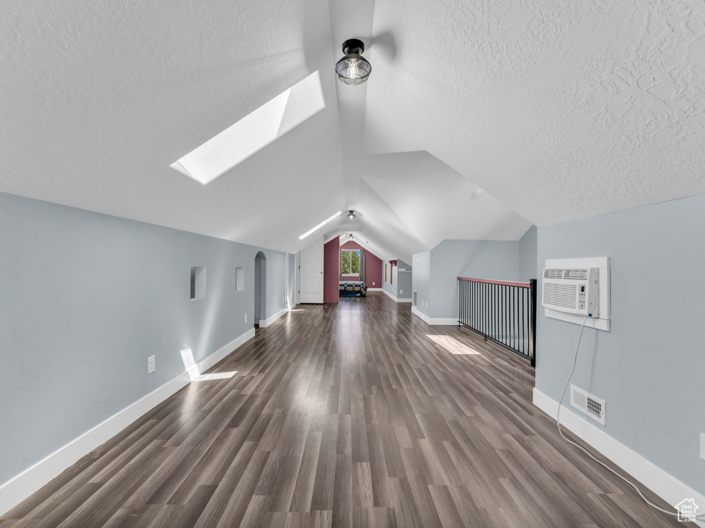 Bonus room with a wall mounted air conditioner, a skylight, a textured ceiling, wood finished floors, and lofted ceiling
