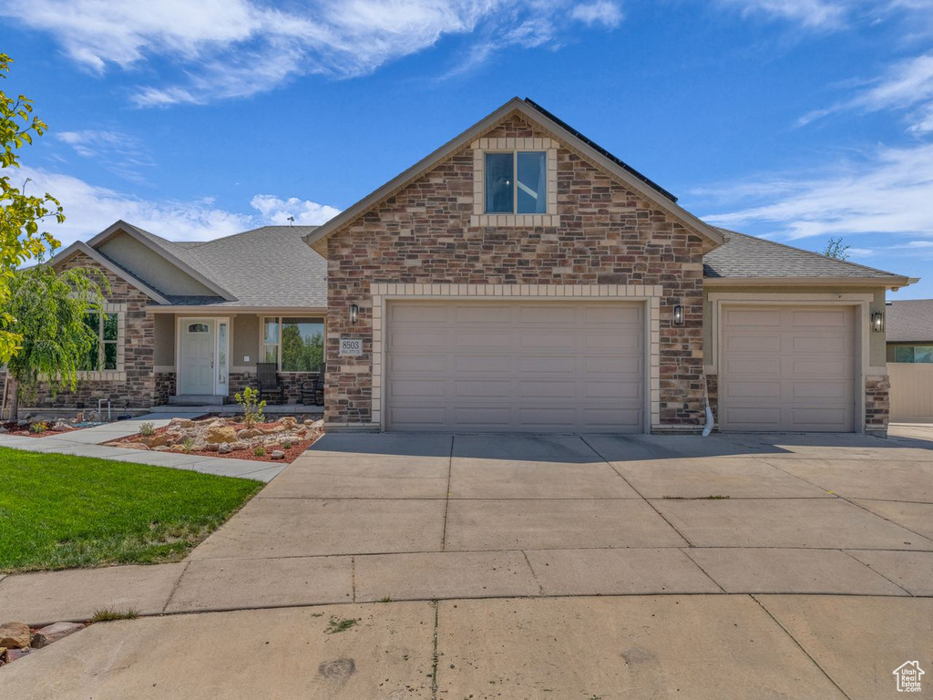 View of front of property with driveway, roof with shingles, a garage, and stone siding