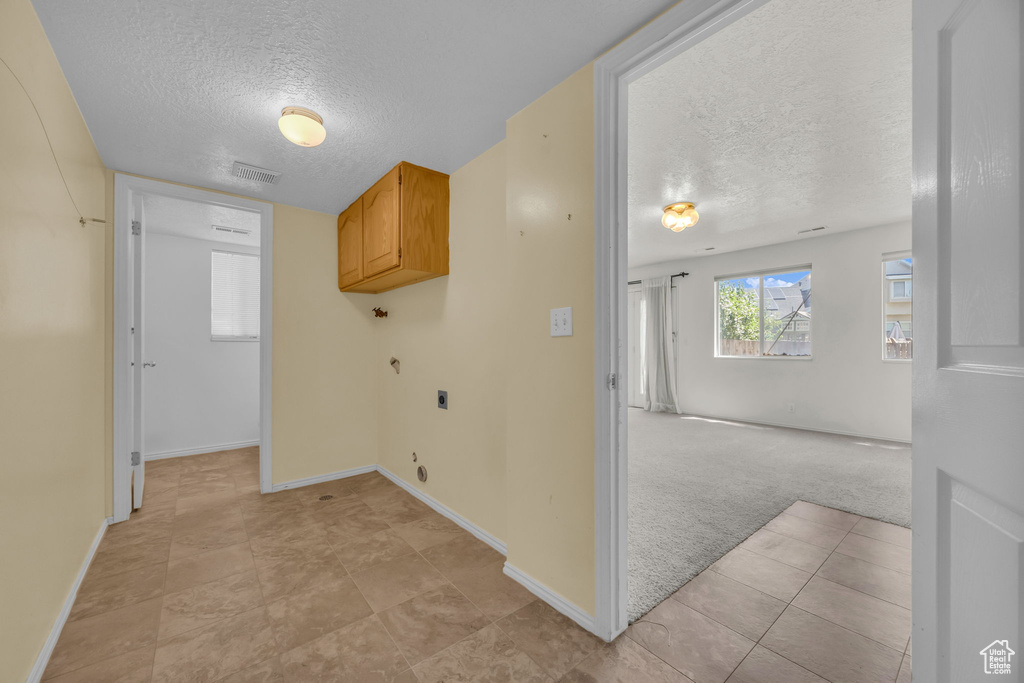 Laundry area with a textured ceiling, cabinet space, electric dryer hookup, light carpet, and light tile patterned floors