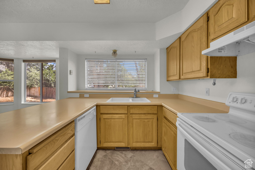 Kitchen featuring white appliances, under cabinet range hood, light countertops, a textured ceiling, and a peninsula
