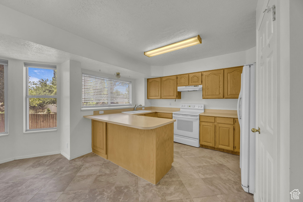 Kitchen featuring white appliances, under cabinet range hood, a peninsula, a textured ceiling, and light countertops