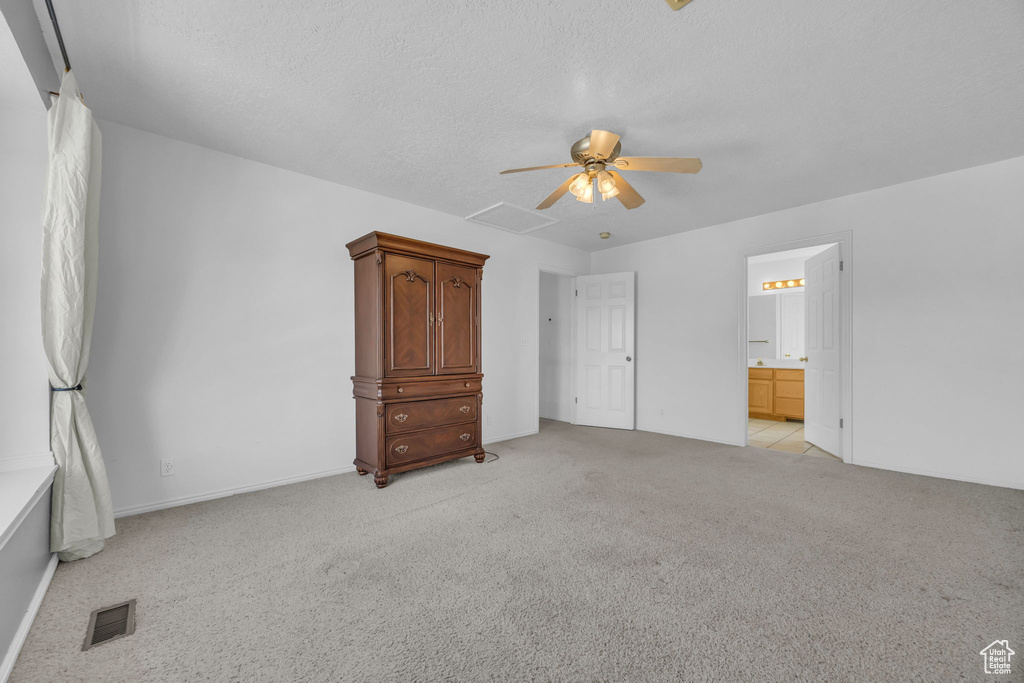 Unfurnished bedroom featuring light colored carpet, ceiling fan, connected bathroom, and a textured ceiling