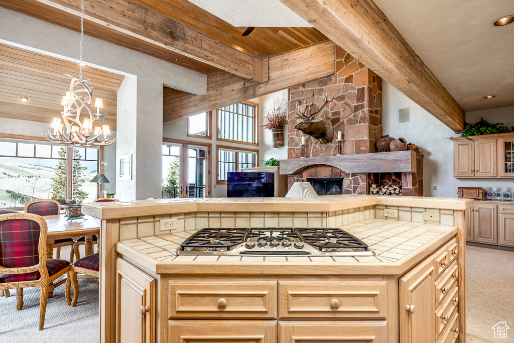 Kitchen featuring tile countertops, stainless steel gas stovetop, light carpet, beam ceiling, and a stone fireplace