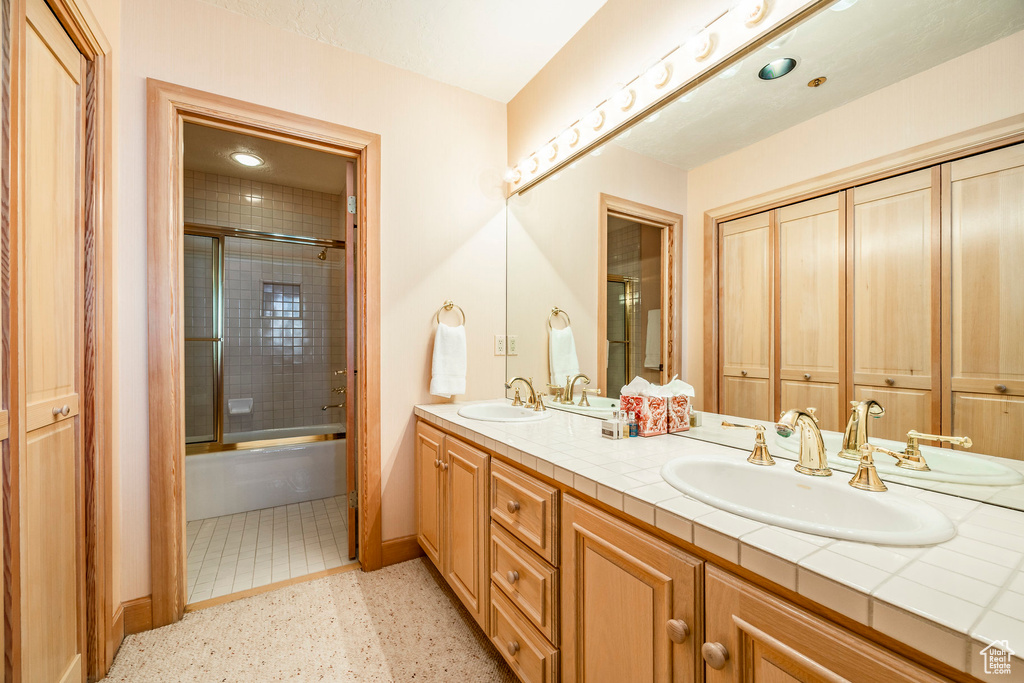 Full bath with double vanity, speckled floor, and combined bath / shower with glass door