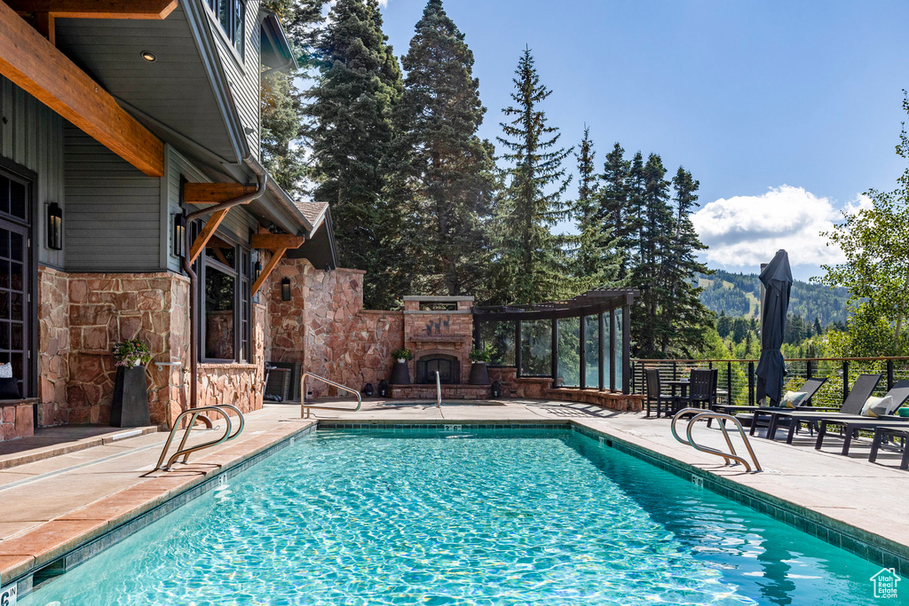 View of pool featuring an outdoor stone fireplace and a patio area
