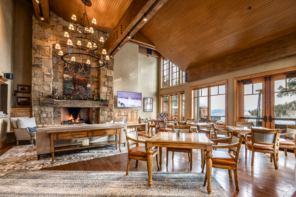 Dining space featuring a wood ceiling with exposed beams, high vaulted ceiling, hardwood / wood-style flooring, a stone fireplace, and a chandelier