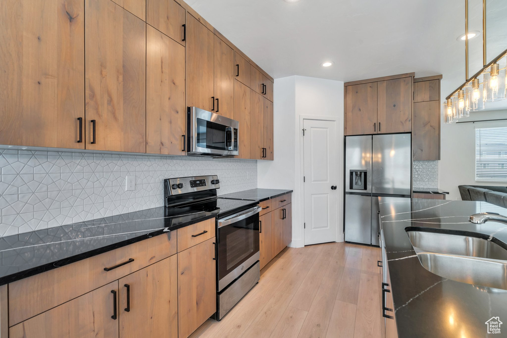 Kitchen with appliances with stainless steel finishes, light wood-style floors, decorative backsplash, dark stone countertops, and hanging light fixtures