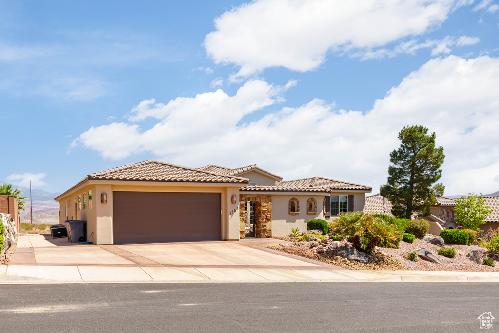 Mediterranean / spanish-style home featuring stucco siding, an attached garage, a tiled roof, and driveway