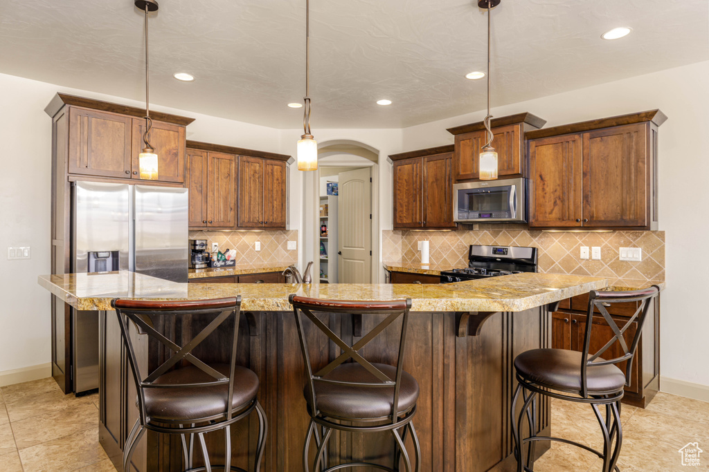 Kitchen featuring appliances with stainless steel finishes, recessed lighting, tasteful backsplash, arched walkways, and a kitchen bar